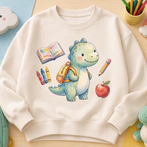 Op de afbeelding: Een crèmekleurige sweater met ronde hals en een aquarelillustratie van een lichtgroene dinosaurus met een oranje rugzak. De dinosaurus is omringd door schoolartikelen, waaronder een open boek, drie kleurpotloden, een potlood en een rode appel.