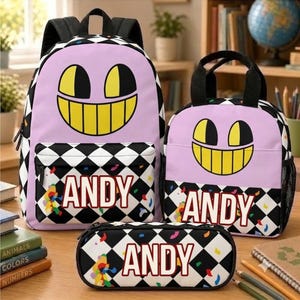 Op de afbeelding: Een bijpassende set bestaande uit een rugzak, een lunchtas en een etui. Elk item is voorzien van een zwart-wit geblokt patroon, een lichtpaars gedeelte met een geel grijnzend gezicht en de naam ANDY in rode letters gedrukt.