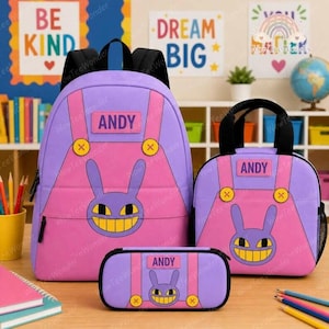 May include: A purple and pink backpack, lunch bag, and pencil case set featuring a cartoon rabbit face graphic with a wide yellow grin. Each item displays the name ANDY on a rectangular patch and includes yellow circular accents resembling buttons.