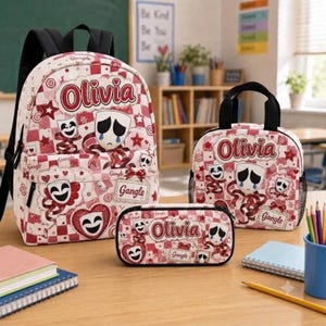 May include: A backpack, lunch bag, and pencil case set featuring a red and white checkered pattern, theater masks, and the name Olivia printed in red. Each item displays a sad mask with blue tears and a happy mask, with the text Gangle included.