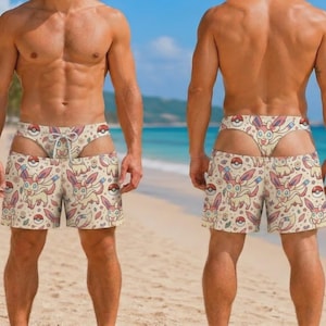 May include: A pair of swim trunks featuring an all-over print of the character Sylveon and red and white Poké Balls on a cream-colored background. The shorts have a drawstring waist and a matching patterned thong-style piece visible above the waistband.
