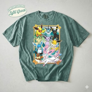 Op de afbeelding: Een lichtgroen t-shirt met korte mouwen en een rechthoekige gouden kaderafbeelding met illustraties van negen kleurrijke fictieve wezens. De tekst "COMFORT COLORS" en "Light Green" staat in een wit ovaal embleem linksboven.