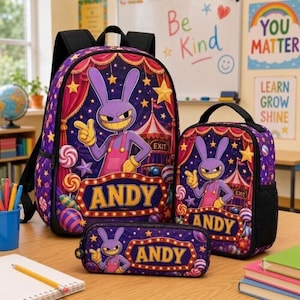 May include: A purple backpack, lunch bag, and pencil case set featuring a cartoon rabbit character in pink overalls, a circus tent background, and the name ANDY printed in yellow letters on a marquee-style sign with colorful candy and star accents.