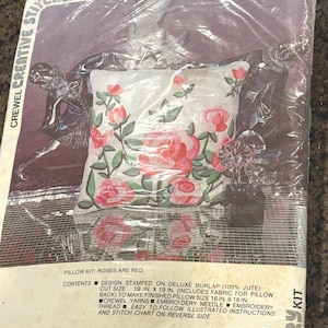 May include: A pillow kit featuring a design of red roses and green leaves on a white background. The kit includes burlap fabric, embroidery thread, and a needle. The finished pillow size will be 16 x 16 inches.