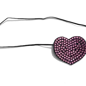 May include: A heart-shaped eye patch with a black elastic band. The patch is covered in small, pink rhinestones. The eye patch is designed to cover one eye.