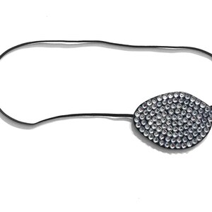 Könnte beinhalten: Eine Augenklappe mit einem schwarzen Band und einem schwarzen, oval geformten Patch, der mit kleinen, klaren Strasssteinen bedeckt ist. Die Augenklappe ist zum Tragen über einem Auge konzipiert.