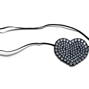 May include: A black eye patch in the shape of a heart, embellished with numerous small, sparkling rhinestones. The heart-shaped patch is attached to a thin, black elastic band, designed to be worn around the head.