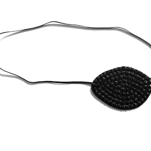 Puede incluir: Parche ocular negro con una parte delantera ovalada y texturizada. Está conectado a una fina banda elástica negra. El parche ocular está diseñado para usarse alrededor de la cabeza. La superficie del parche ocular parece irregular.