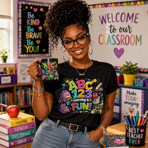 May include: A black t-shirt and matching mug featuring colorful school-themed graphics with the text ABC 123 Learning is FUN. The design includes illustrations of a backpack, books, an apple, and pencils. The mug is held in one hand.