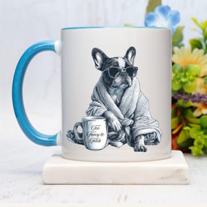 May include: White ceramic mug with a blue handle and rim. The mug features a black and white illustration of a French Bulldog wearing sunglasses and a robe, with a small mug that says "Too Fancy to Fetch."