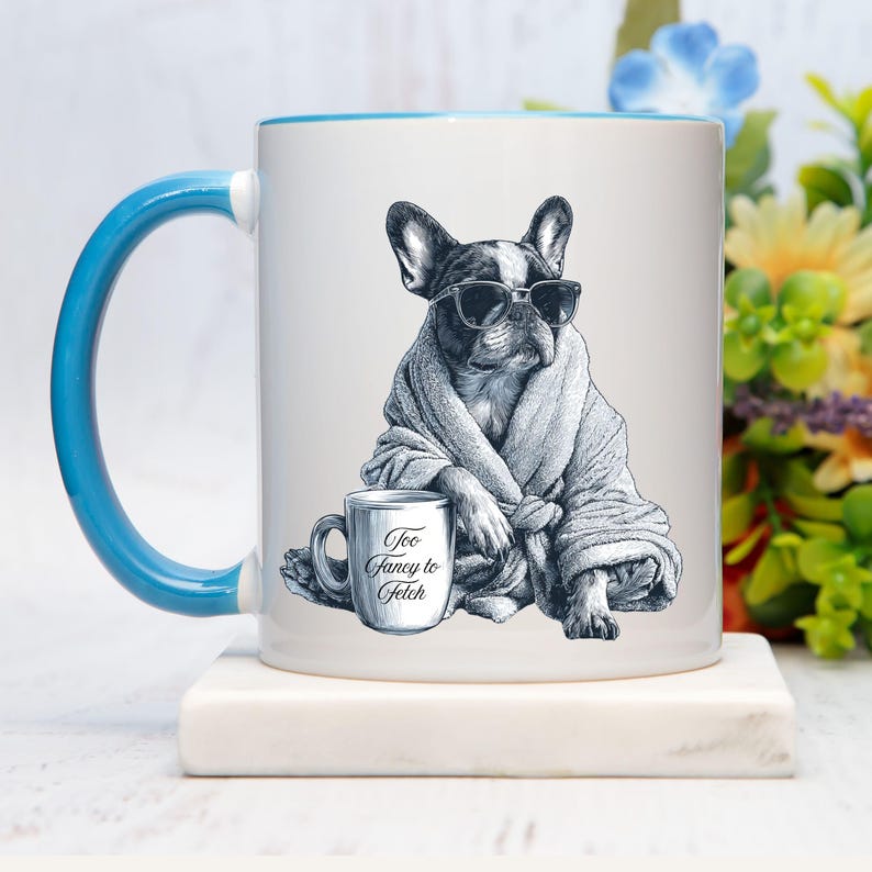 May include: White ceramic mug with a blue handle and rim. The mug features a black and white illustration of a French Bulldog wearing sunglasses and a robe, with a small mug that says "Too Fancy to Fetch."