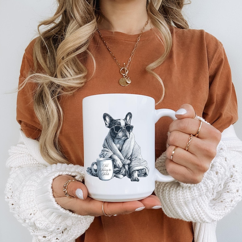 May include: White ceramic mug featuring a black and white illustration of a French Bulldog wearing sunglasses and a robe. The mug also has the text "Too Fancy to Fetch" on the mug and a smaller cup.