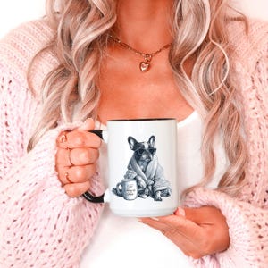 May include: White ceramic mug with a black interior and handle. The mug features a graphic of a French bulldog wearing sunglasses and a robe, with a small coffee cup. Text on the cup reads "Too Funny to Fold".