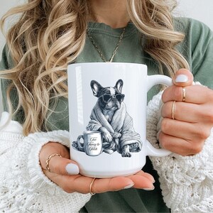 May include: White ceramic mug featuring a black and white illustration of a French Bulldog wearing sunglasses and a robe, with a coffee cup that reads "Too Fancy to Fetch". The mug has a large handle.