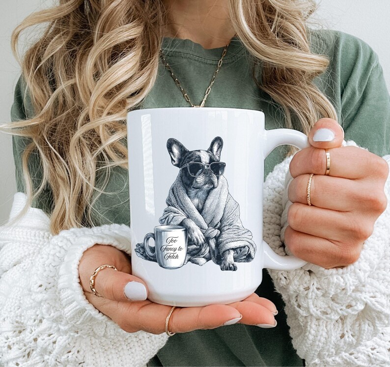 May include: White ceramic mug featuring a black and white illustration of a French Bulldog wearing sunglasses and a robe, with a coffee cup that reads "Too Fancy to Fetch". The mug has a large handle.