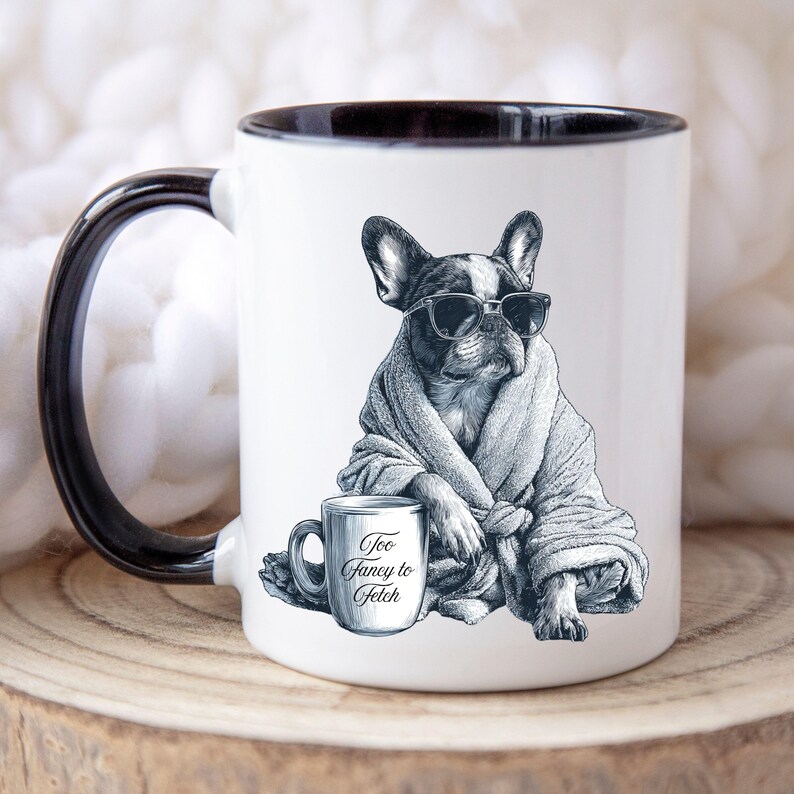 May include: White ceramic mug with a black interior and handle. The mug features a black and white illustration of a French Bulldog wearing sunglasses and a robe. A smaller mug with the text "Too Fancy to Fetch" is also in the image.