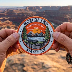 May include: A circular embroidered patch featuring a landscape illustration of mountains, a lake, and pine trees under a sunset. The text reads WORLDS END PENNSYLVANIA 1932 STATE PARK. The patch has a white center, a bright orange border, and black text.