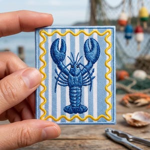 May include: A rectangular embroidered patch featuring a centered dark blue lobster on a light blue and white vertical striped background, framed by a bright yellow wavy border with a light blue stitched edge on all four sides of the patch.