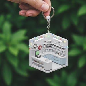 May include: A miniature pharmacy keychain with a detailed interior, including shelves of medicine bottles, a computer, and a red cross symbol. The keychain is held by a hand against a blurred green background. The text "Dr. Thomas" is visible.
