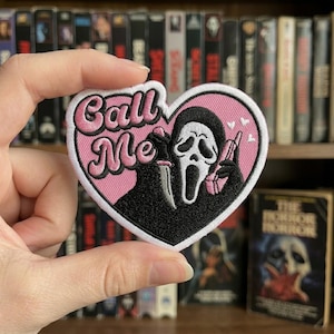 May include: A heart-shaped patch with the text "Call Me" in pink script. The patch features a black and white Ghostface character holding a knife and making a peace sign, set against a pink background.