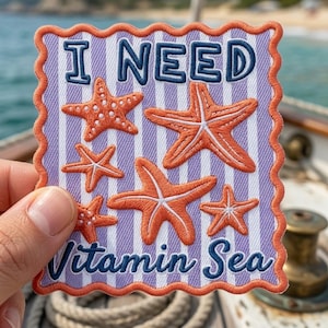 May include: A rectangular embroidered patch with a scalloped orange border featuring a light purple and white vertical striped background. The text I NEED Vitamin Sea is stitched in dark blue, accompanied by six orange starfish of varying sizes.