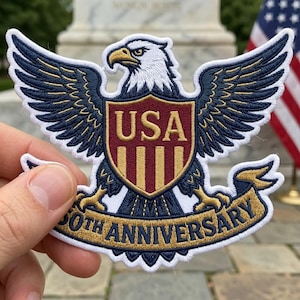 May include: Embroidered patch featuring a majestic eagle with outstretched wings, holding a shield with "USA" and vertical stripes. A banner below reads "50TH ANNIVERSARY". The patch is in shades of blue, gold, red, and white.
