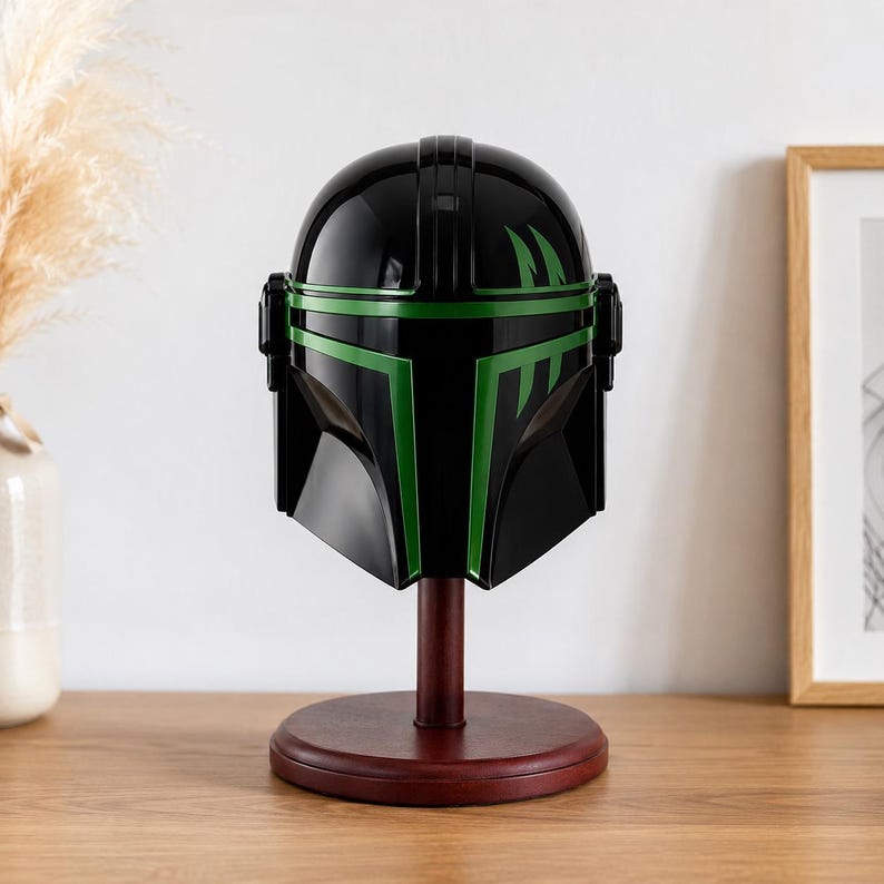 Puede incluir: Un casco negro con detalles verdes, exhibido sobre un soporte de madera. El casco presenta un acabado brillante y un dise&ntilde;o angular distintivo, con rayas y marcas verdes. El soporte es de color marr&oacute;n oscuro, proporcionando una base contrastante.