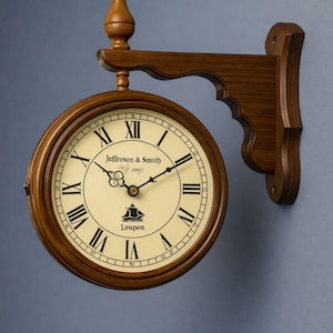 May include: A double-sided wall-mounted clock with a dark wood frame and bracket. The cream-colored face features black Roman numerals, black hands, and the text Jefferson & Smith along with a ship icon and the word Loupon printed in the center.