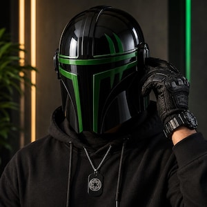 Puede incluir: Un casco negro con detalles verdes, con un acabado brillante. El casco tiene una visera y forma parte de un disfraz. La persona lleva una sudadera con capucha negra y un collar con una placa de identificaci&oacute;n. La persona tambi&eacute;n lleva un guante negro y un reloj.