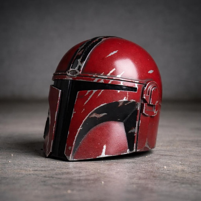 May include: A weathered, red helmet with black accents and silver scratches. The helmet has a rounded top with a black stripe and a rectangular visor. The design suggests a sci-fi or cosplay theme.