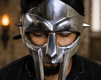 May include: A polished silver-colored metal mask featuring a prominent brow ridge, a central nose bridge, and two vertical cheek plates. The mask includes small, pointed spikes on each side and a wide horizontal eye opening across the upper section.