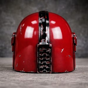 May include: A red helmet with a black stripe down the center and silver accents. The helmet has a weathered appearance with visible scratches and wear. The design includes side details and a lower section with a textured pattern.