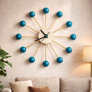 May include: A modern wall clock with a cream-colored face and black hands. The clock features gold-colored spokes with teal blue spheres at the ends, creating a unique, starburst design. The clock is mounted on a light-colored wall.