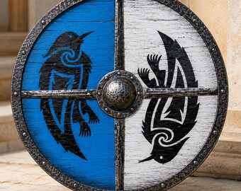 May include: A circular wooden shield divided into blue and white halves, featuring a black raven silhouette on each side. The shield has a dark, hammered metal rim and a central metal boss, with a cross-shaped metal reinforcement bar across the face.