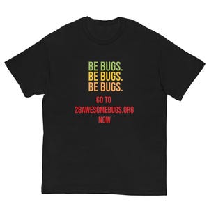 May include: Black t-shirt featuring the text "BE BUGS" in green, yellow, and red, repeated three times. Underneath, the text "GO TO 28AWESOMEBUGS.ORG NOW" is printed in red. The shirt is made of a soft material.