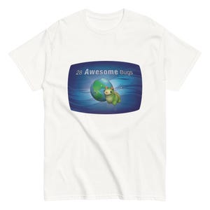 Op de afbeelding: Een wit T-shirt met korte mouwen en een centrale rechthoekige afbeelding op een blauwe achtergrond, met een kleine groene rups, een wereldbol en de witte tekst 28 Awesome Bugs bovenaan het ontwerp.