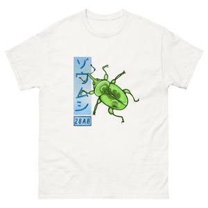 Könnte beinhalten: Weißes T-Shirt mit einer grünen Käfer-Illustration und schwarzen Umrissen. Das Design enthält japanische Schriftzeichen und die Nummer "28AB" in einem blauen Rechteck. Das Shirt besteht aus einem weichen, bequemen Material.