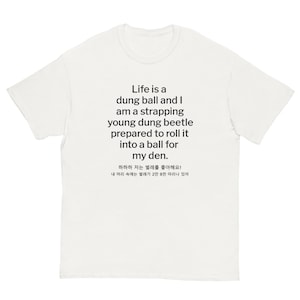 Könnte beinhalten: Weißes T-Shirt mit schwarzem Text. Der Text lautet: "Life is a dung ball and I am a strapping young dung beetle prepared to roll it into a ball for my den." Zusätzlicher Text auf Koreanisch ist ebenfalls vorhanden.