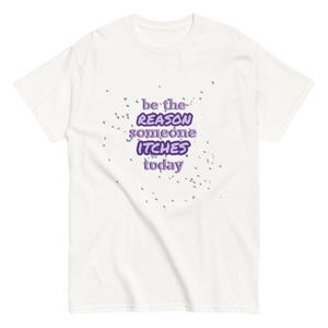 May include: White t-shirt featuring the purple text: "be the REASON someone ITCHES today". The shirt has a crew neck and short sleeves. Small purple dots are scattered around the text.