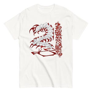Peut inclure: Un t-shirt blanc à manches courtes avec une grande impression graphique sur le devant. Le motif représente une créature centipède segmentée et stylisée en blanc avec des contours et des pattes rouge foncé, à côté d'un texte vertical complexe.