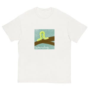 May include: White t-shirt featuring a square graphic of a yellow-green caterpillar on a brown branch against a blue background. The word "incheresting" is printed below the graphic. The t-shirt has short sleeves and a crew neck.