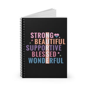 May include: A spiral-bound notebook with a black cover. The cover features the word "NURSE" vertically, with the words "STRONG, BEAUTIFUL, SUPPORTIVE, BLESSED, WONDERFUL" arranged around it in various colors. A heart and star graphic are also included.