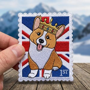 May include: Embroidered patch featuring a smiling corgi wearing a crown, set against a Union Jack background. The patch is designed to resemble a postage stamp, with the text "1ST" at the bottom. The corgi has brown and white fur.