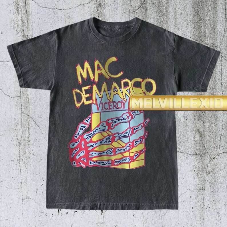 以下が含まれることがあります： 「MAC DEMARCO」の文字が黄色で、下に「VICEROY」と書かれた濃いグレーのTシャツ。赤と白の骸骨の手が箱を持っています。このシャツはヴィンテージで使い古された外観をしています。