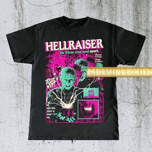 Peut inclure: T-shirt noir avec le titre du film "HELLRAISER" en rose et blanc. Le graphisme comprend un personnage au visage pâle et une grille d'images. Le texte comprend "He'll tear your soul apart" et "JESUS WEPT."