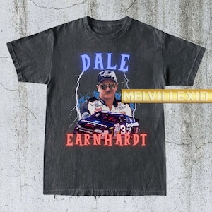 Könnte beinhalten: Dunkelgraues T-Shirt mit einem Porträt von Dale Earnhardt und dem Text "DALE EARNHARDT" in blauen und roten Neonbuchstaben. Das Design umfasst ein Rennauto und Blitze.