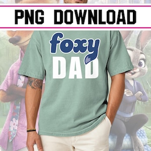 Könnte beinhalten: Ein hellgrünes T-Shirt mit dem Text "foxy DAD" in Weiß und Blau. Das Wort "foxy" ist in einer stilisierten Schriftart mit einer Fuchsschwanzgrafik gehalten. Das Shirt ist kurzärmlig und scheint aus einem weichen Material zu sein.