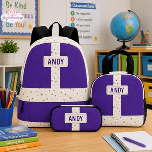 Op de afbeelding: Een paarse rugzak, een bijpassende lunchtas en een etui, allemaal voorzien van een wit kruispatroon met grijze spikkels en de naam ANDY in het wit gedrukt op een rechthoekige patch aan de voorzijde van elk stoffen item.
