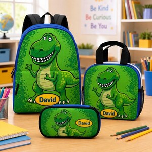 Puede incluir: Un conjunto de mochila, bolsa de almuerzo y estuche de color verde brillante con un personaje de dibujos animados de tiranosaurio rex. Cada artículo muestra el nombre David en una insignia ovalada amarilla. Las bolsas tienen correas negras.