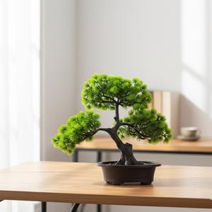 Puede incluir: Un pequeño bonsái artificial en una maceta marrón oscuro. El árbol tiene un tronco oscuro y un follaje verde brillante y texturizado. El bonsái se exhibe sobre una mesa de madera marrón claro, con un fondo borroso de una habitación.